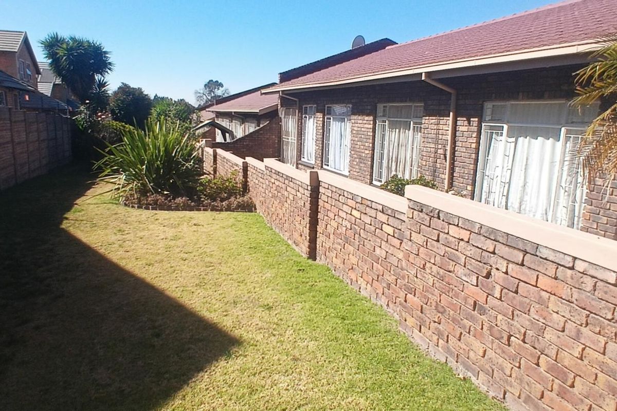A view of the rear exterior of the townhouse, featuring a brick facade, tiled roof, and a private lawn area with boundary walling.