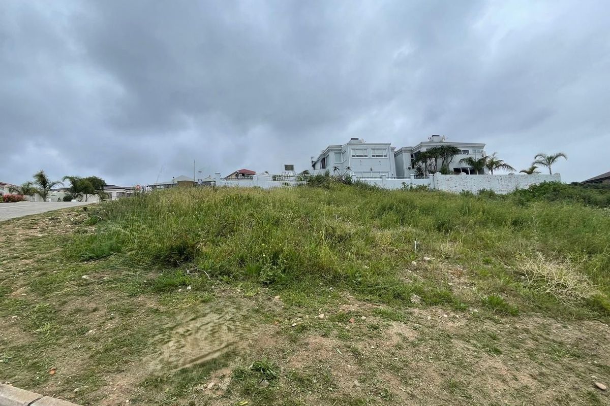 A view of a vacant residential plot of land with natural grass cover, situated in a developed neighborhood.