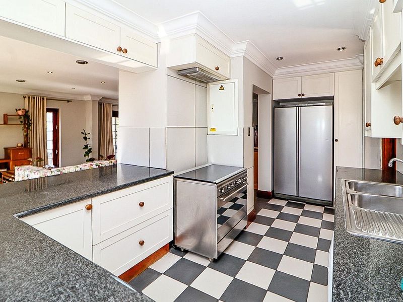 A functional kitchen featuring granite countertops, white cabinetry, a stainless steel stove with extractor fan, and classic checkerboard floor tiling.