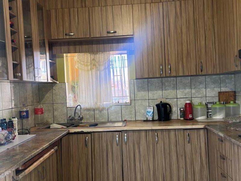 A functional kitchen featuring wood-grain laminate cabinetry, tiled backsplash, and laminate countertops with a stainless steel sink.