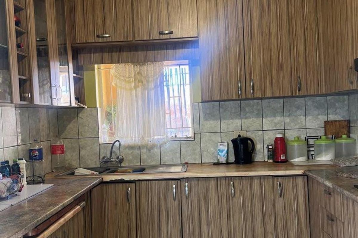 A functional kitchen featuring wood-grain laminate cabinetry, tiled backsplash, and laminate countertops with a stainless steel sink.