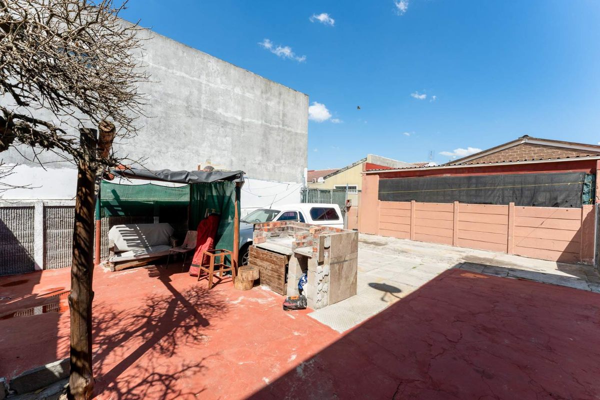 Rear outdoor area featuring a paved patio, a built-in brick braai, and perimeter boundary walls, offering potential for landscaping and entertainment space development.
