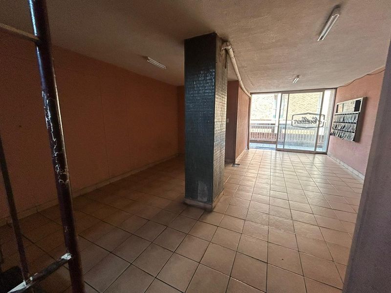 A vacant ground floor lobby or entrance area featuring tiled flooring, a central structural column, and wall-mounted mailboxes leading to an exterior entrance.
