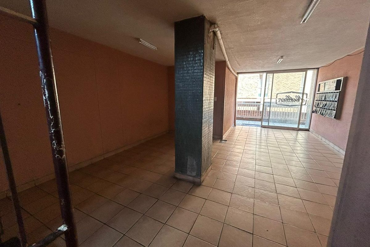 A vacant ground floor lobby or entrance area featuring tiled flooring, a central structural column, and wall-mounted mailboxes leading to an exterior entrance.