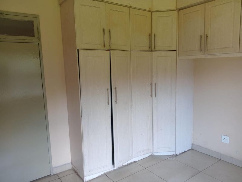 A vacant bedroom featuring built-in wooden cupboards, tiled flooring, and neutral wall finishes, offering a blank canvas for potential updates.