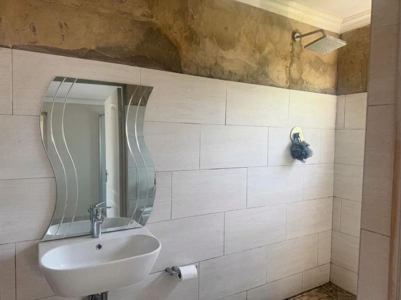 A bathroom featuring a wall-mounted basin and shower head, currently requiring completion of wall plastering and finishing above the tiled area.