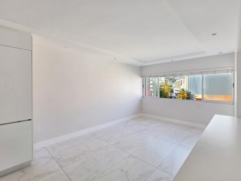 A bright, empty living area featuring modern marble-look floor tiles, recessed ceiling lighting, and built-in cabinetry with a view through the window.