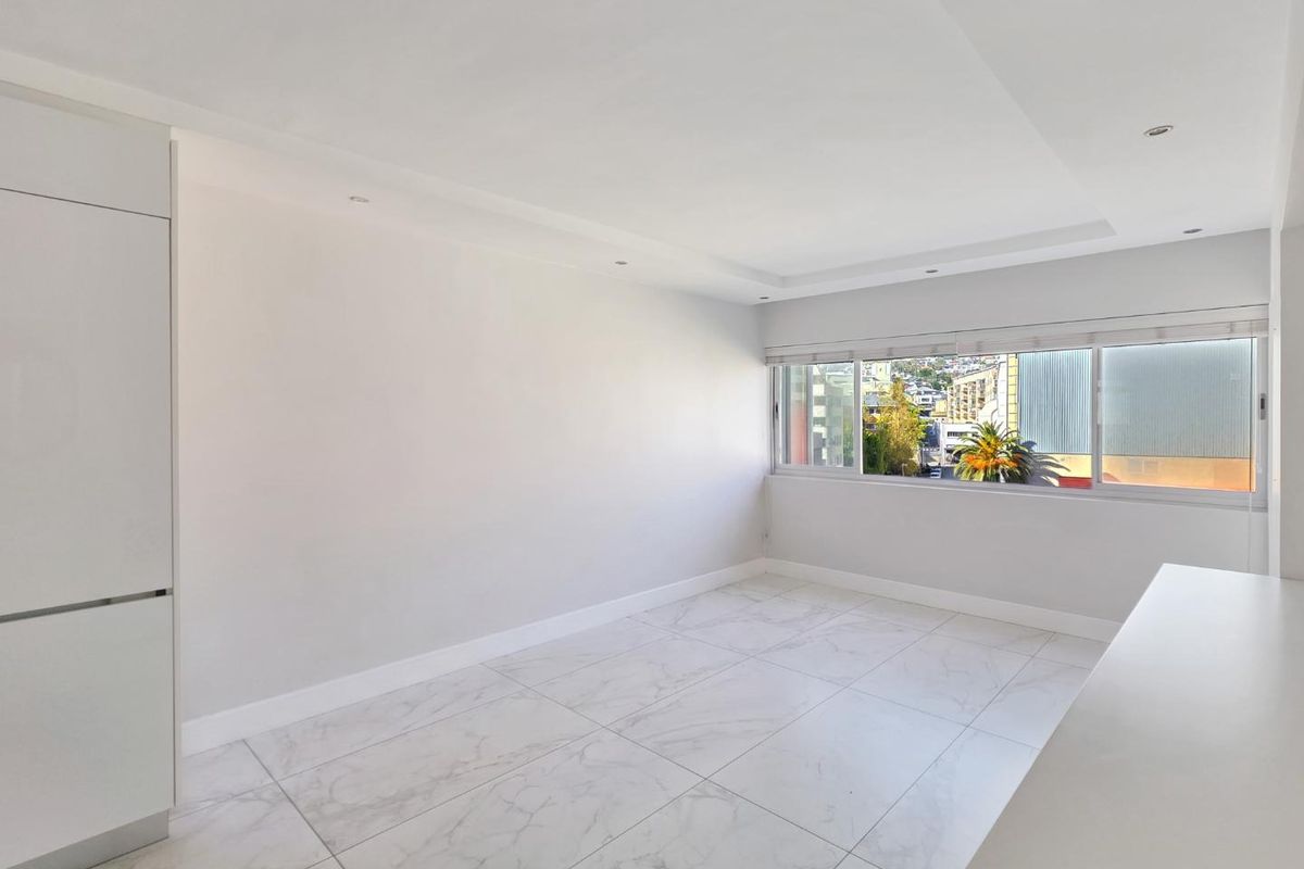 A bright, empty living area featuring modern marble-look floor tiles, recessed ceiling lighting, and built-in cabinetry with a view through the window.