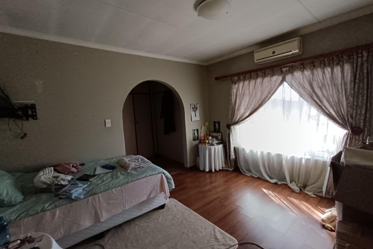 A bedroom featuring laminate flooring, an arched doorway leading to a built-in cupboard, and a wall-mounted split-system air conditioner.