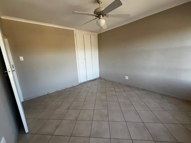 An empty bedroom featuring neutral wall paint, tiled flooring, built-in cupboards, and a ceiling fan.