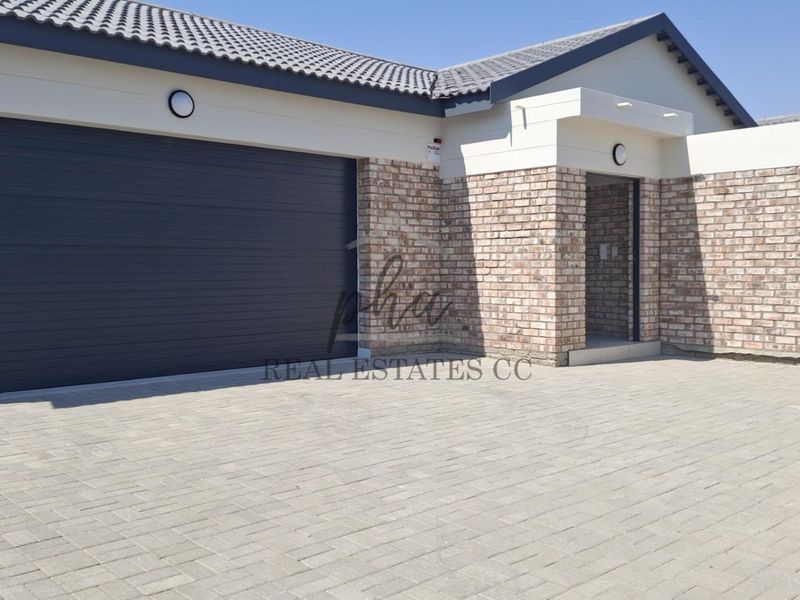 Modern front elevation featuring a brick facade, tiled roof, automated garage door, and a paved driveway with secure entrance.