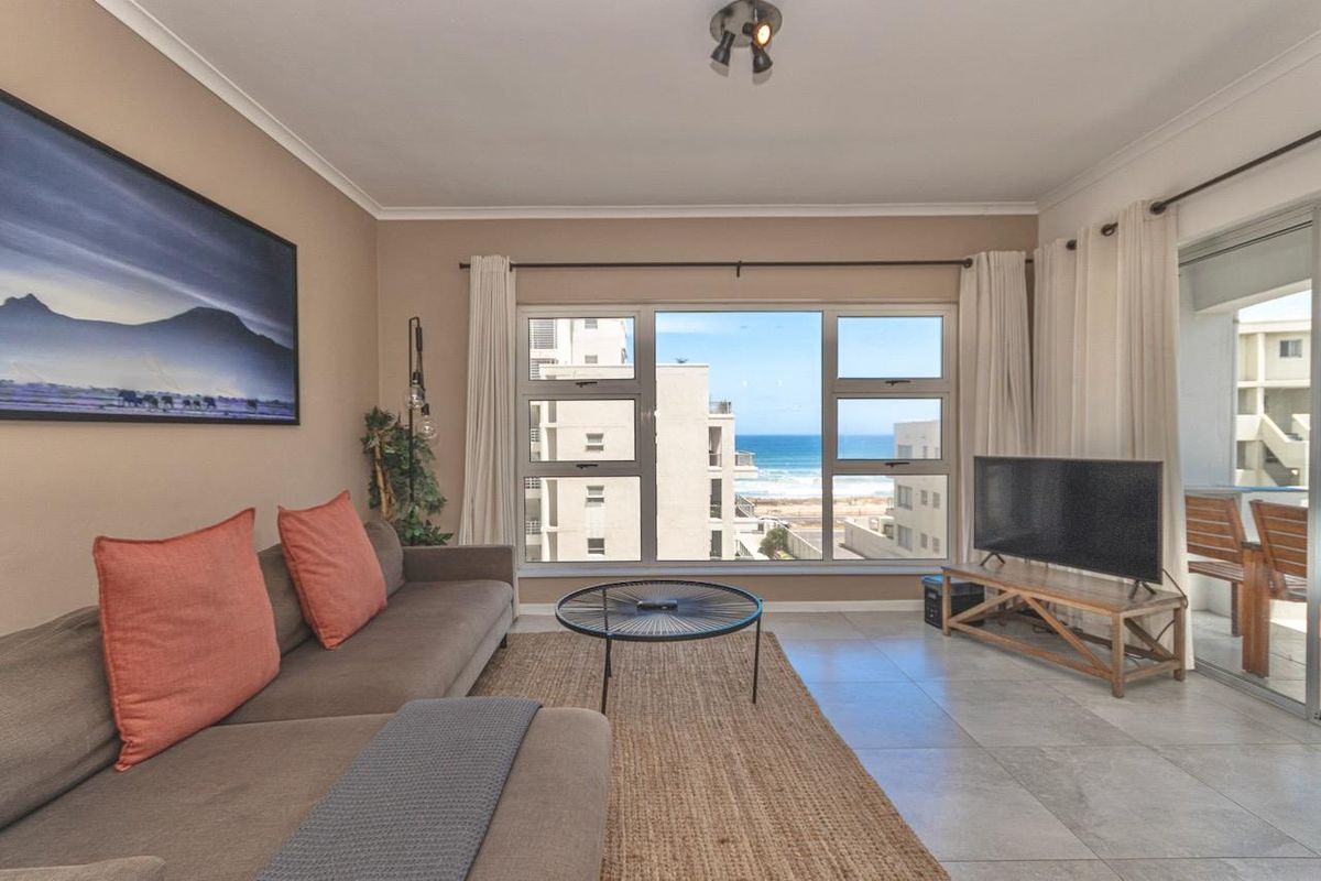 A bright living room featuring large windows with ocean views, tiled flooring, and direct access to a private balcony.