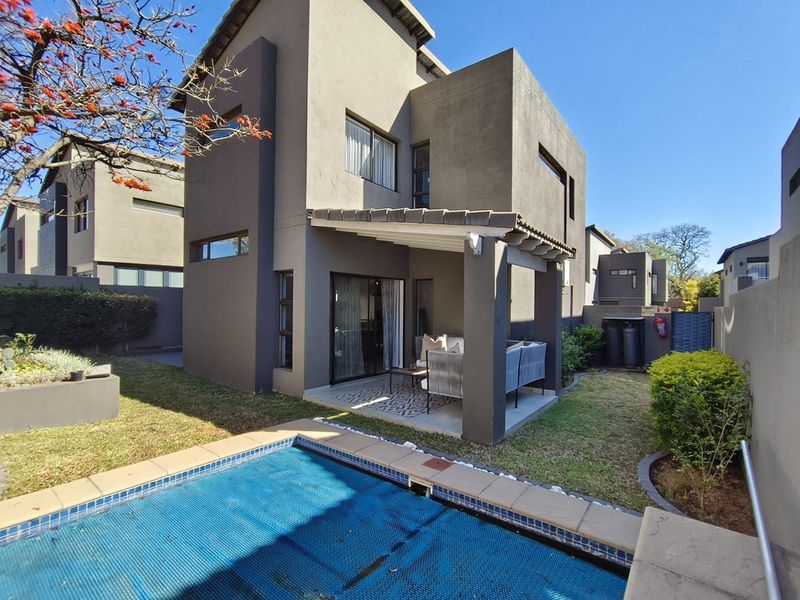 Rear view of a modern double-story house featuring a covered patio, a swimming pool with a cover, and a landscaped garden area.