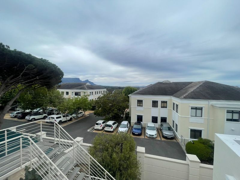 Elevated view of the office complex exterior, featuring a paved parking area, landscaped trees, and a staircase leading to the building entrance.