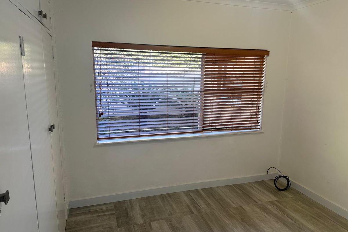 An empty bedroom featuring light-toned laminate flooring, built-in wardrobe storage, and timber venetian blinds.