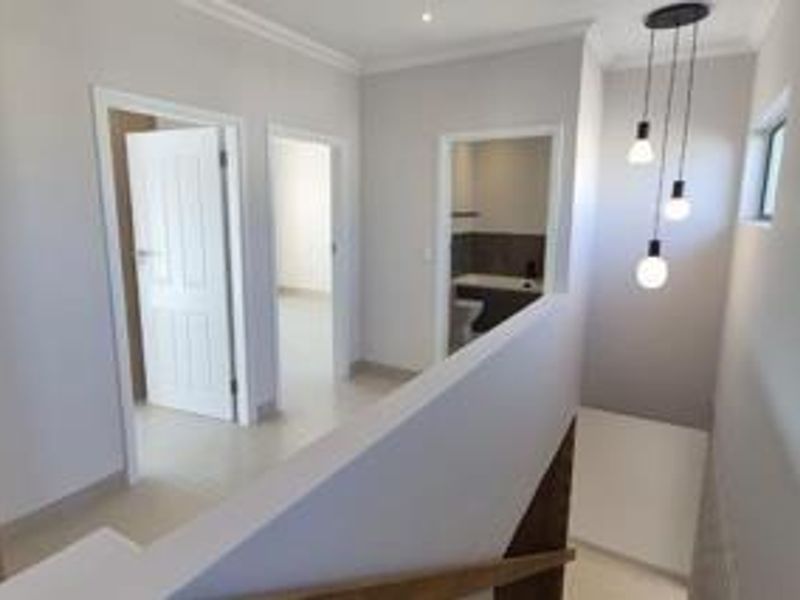 A bright, modern upstairs landing area featuring tiled flooring, contemporary pendant lighting, and access to adjacent bedrooms and a bathroom.