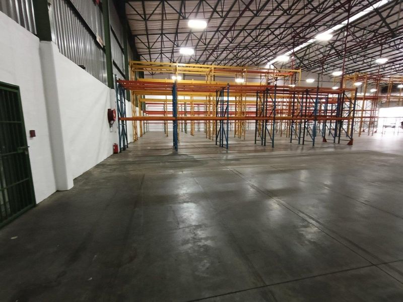 Spacious industrial warehouse featuring high ceilings with exposed steel trusses, concrete flooring, and extensive built-in racking systems for storage.