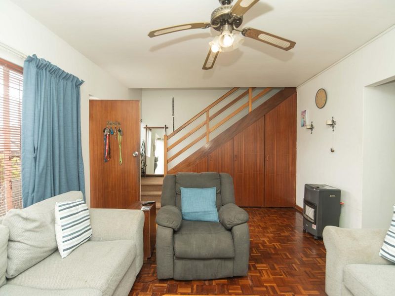 Living room featuring classic parquet flooring, a ceiling fan, and integrated under-stair storage cabinetry with wooden finishes.