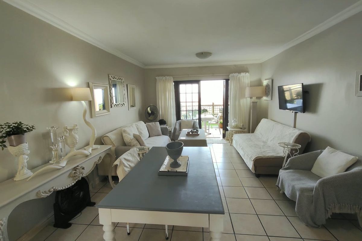 A spacious living area featuring tiled flooring, cove cornicing, and a sliding glass door providing access to an outdoor balcony.