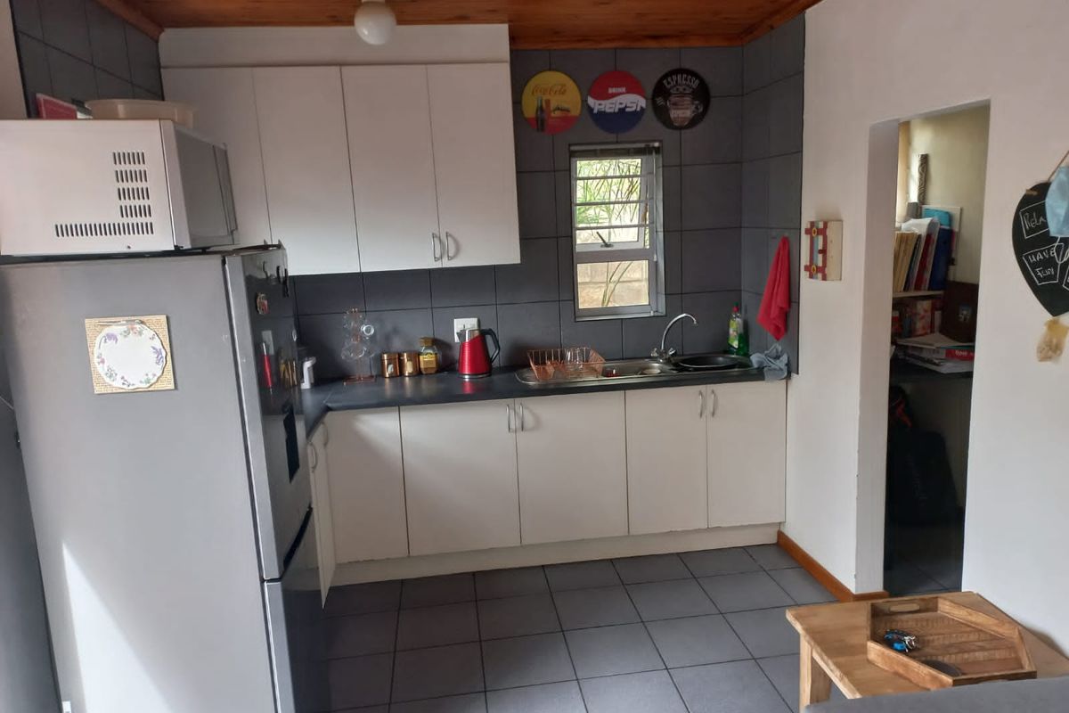 A functional kitchen featuring white cabinetry, dark tiled backsplash, tiled flooring, and a timber ceiling, providing a practical workspace with integrated sink and storage.