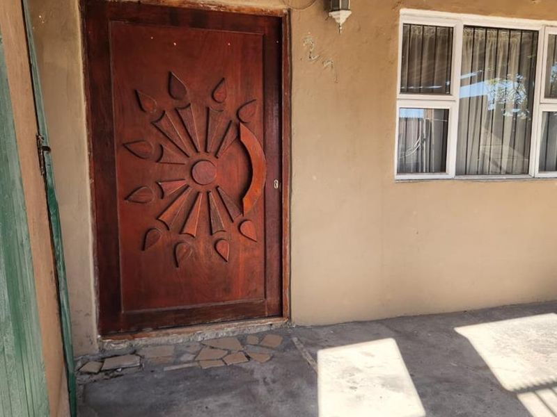 Covered patio area featuring a decorative timber entrance door, aluminium window frames, and a concrete floor under a corrugated iron roof structure.