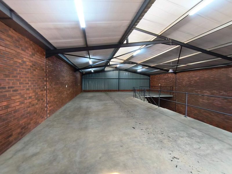 Spacious industrial mezzanine area featuring exposed brick walls, steel roof trusses, and durable concrete flooring, suitable for storage or workshop use.