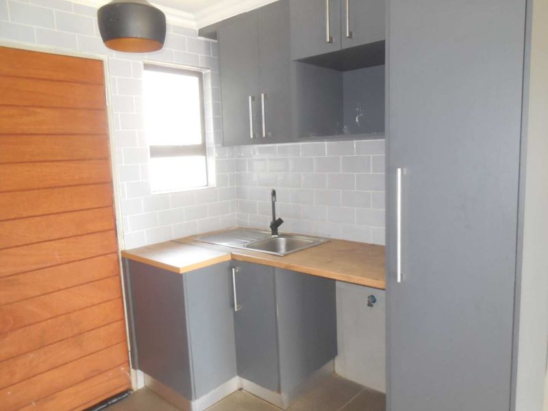 A compact, modern kitchen featuring grey cabinetry, subway tile backsplash, wooden countertops, and a stainless steel sink with a black faucet.