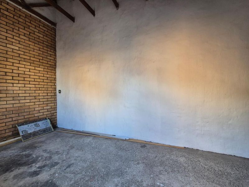 A spacious, unfinished garage area featuring exposed brickwork, timber rafters, and a concrete floor, offering a blank canvas for storage or workshop use.
