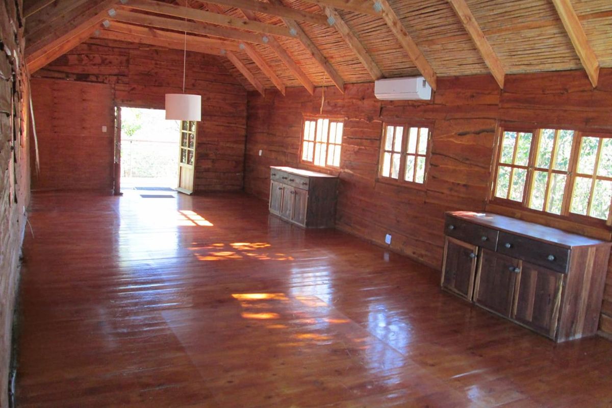 Spacious living area featuring warm timber walls, polished wooden floors, exposed rafters, and a thatched ceiling, creating a rustic and inviting atmosphere.