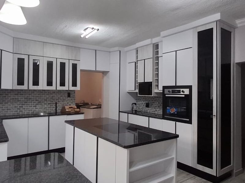 Modern kitchen featuring sleek white cabinetry with black trim, granite countertops, a central island, and a subway tile backsplash.