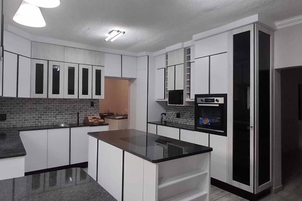Modern kitchen featuring sleek white cabinetry with black trim, granite countertops, a central island, and a subway tile backsplash.