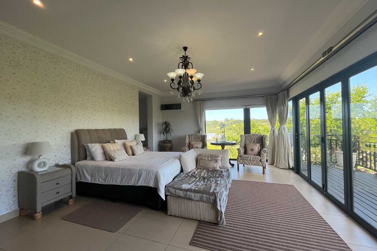 Spacious bedroom featuring large glass sliding doors opening onto a deck, recessed lighting, a decorative chandelier, and neutral tiled flooring.