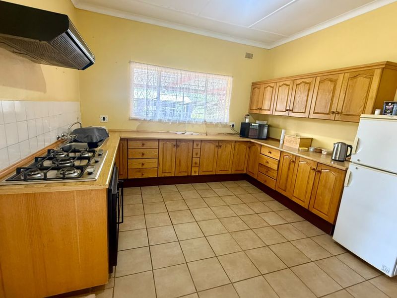 A functional kitchen featuring wooden cabinetry, a gas hob with extractor fan, tiled flooring, and a double sink with a tiled backsplash.