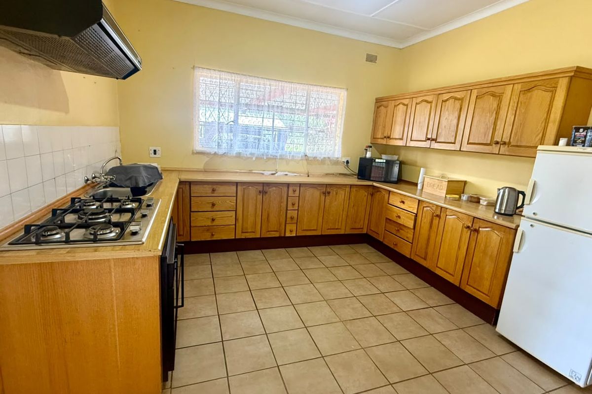 A functional kitchen featuring wooden cabinetry, a gas hob with extractor fan, tiled flooring, and a double sink with a tiled backsplash.