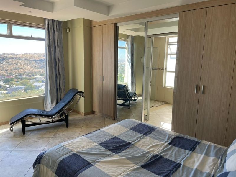 Spacious bedroom featuring built-in cupboards, tiled flooring, and an en-suite bathroom, complemented by large windows offering expansive scenic views.