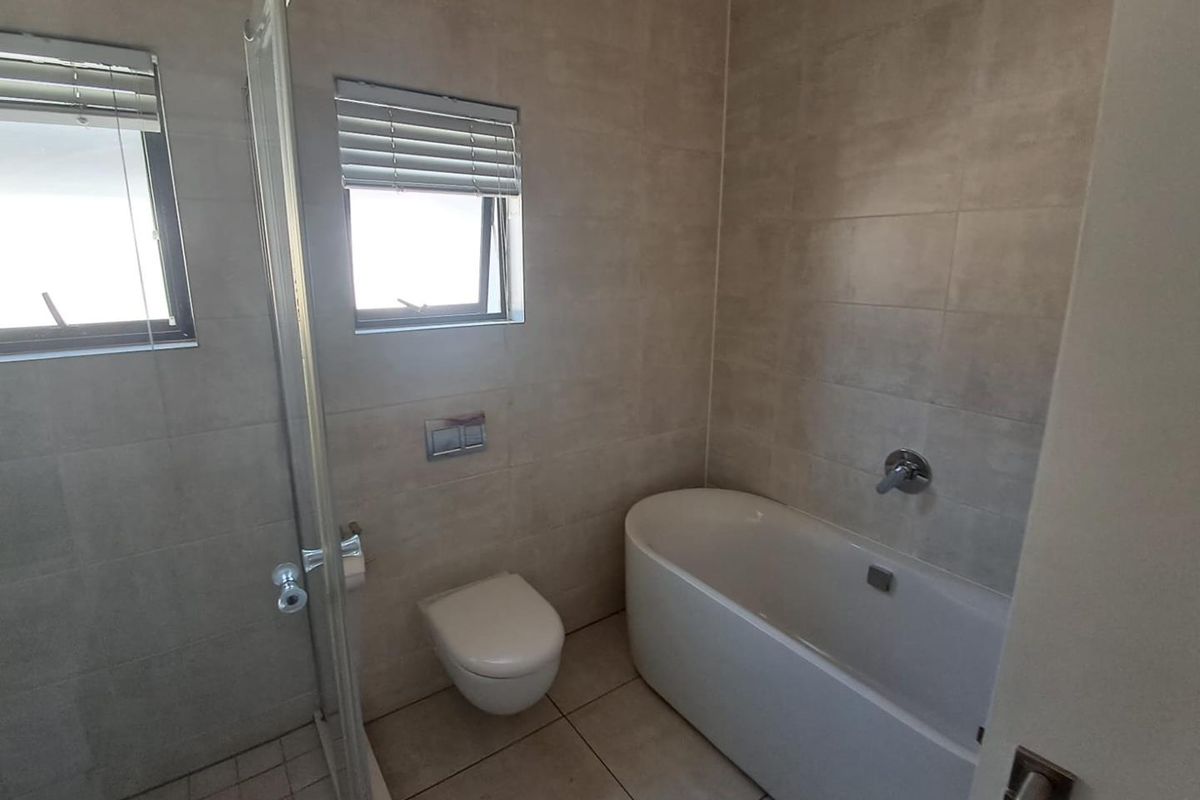 Modern bathroom featuring a wall-mounted toilet, a sleek freestanding bathtub, and a separate glass-enclosed shower with neutral ceramic tiling throughout.