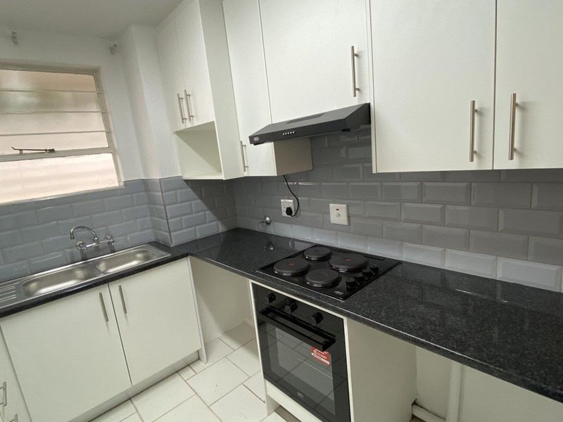 A clean, modern kitchen featuring white cabinetry, dark granite countertops, a subway tile backsplash, and integrated appliances including an oven and hob.