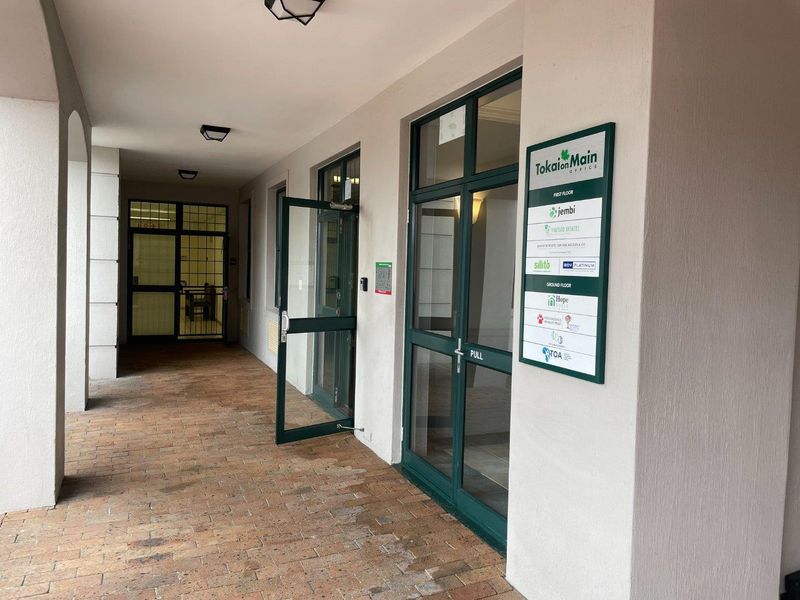 Covered entrance walkway featuring brick paving, glass-paneled doors, and a building directory sign for the Tokai on Main office complex.