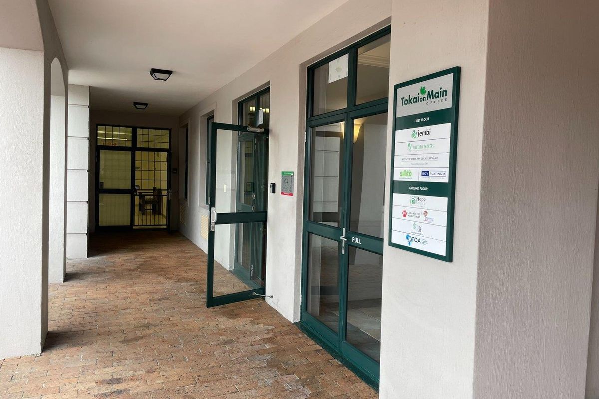 Covered entrance walkway featuring brick paving, glass-paneled doors, and a building directory sign for the Tokai on Main office complex.