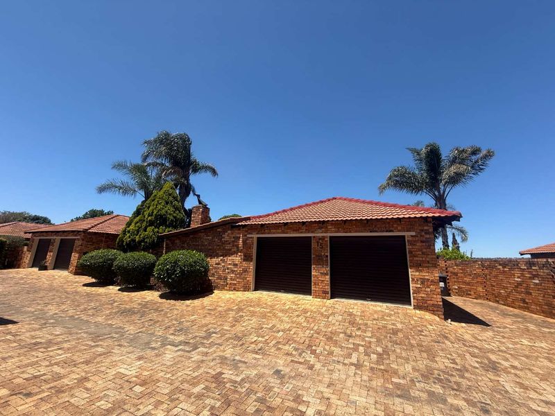 Front exterior view of a facebrick townhouse featuring a double garage and paved driveway under a clear blue sky.