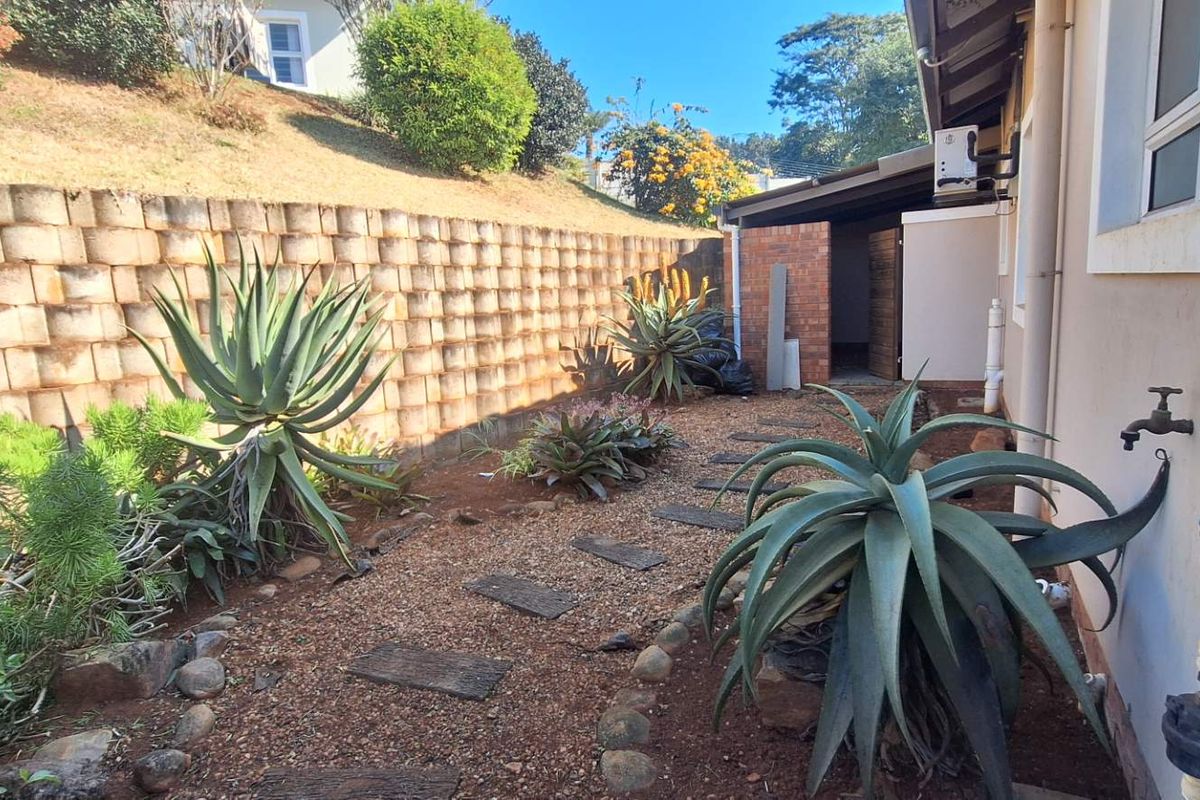 Rear garden area featuring a retaining wall, gravel landscaping, paved stepping stones, and external utility connections.