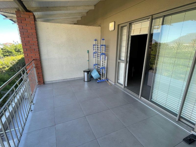 A spacious covered balcony featuring modern grey floor tiles, a metal balustrade, and direct access to the interior through a large sliding glass door.
