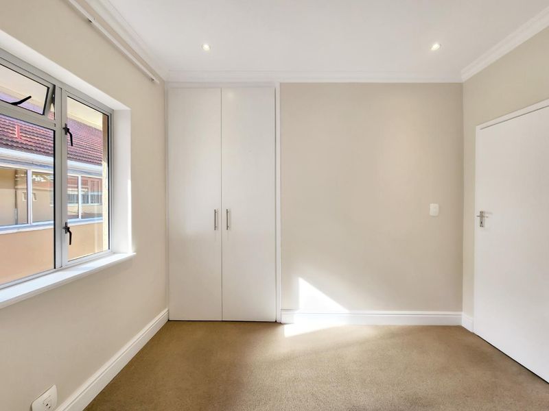 A bright and clean bedroom featuring neutral carpeting, built-in cupboards, and recessed downlighting, offering a versatile space ready for personalization.