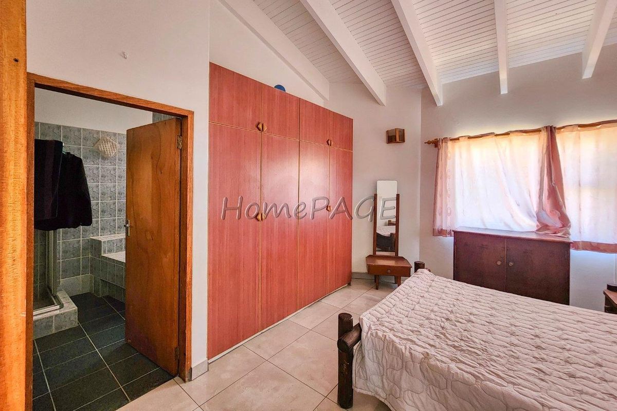 Bedroom featuring high vaulted ceilings, built-in wooden wardrobes, and an en-suite bathroom with tiled finishes.