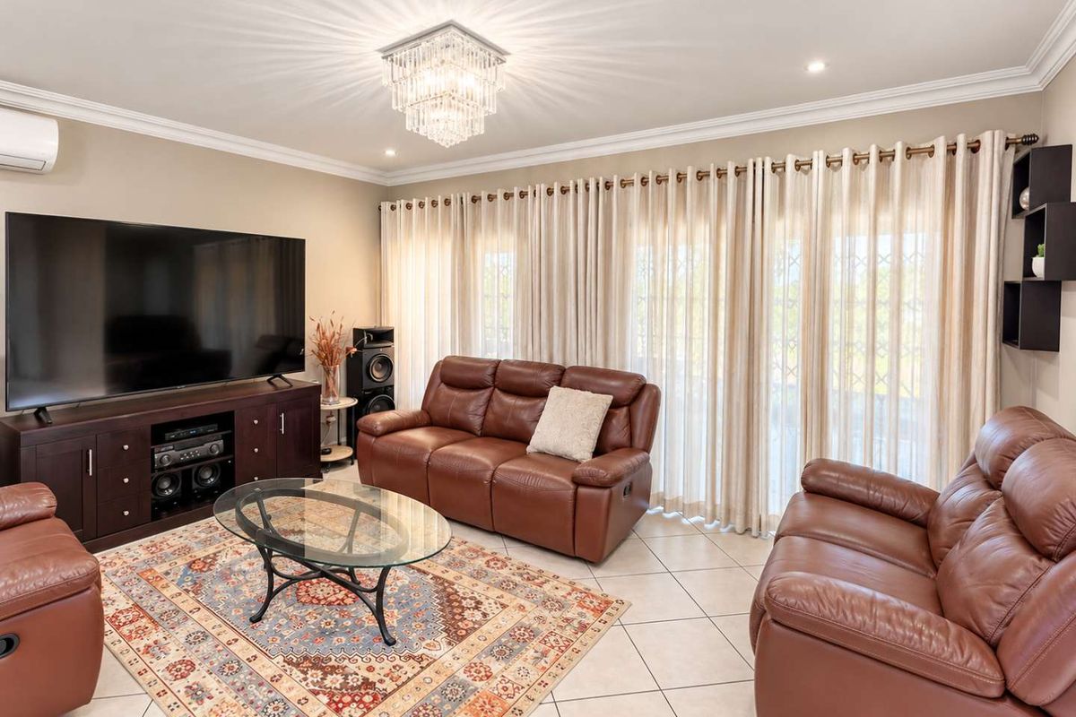 A well-maintained living room featuring tiled flooring, crown molding, a crystal chandelier, and large sliding glass doors providing natural light.