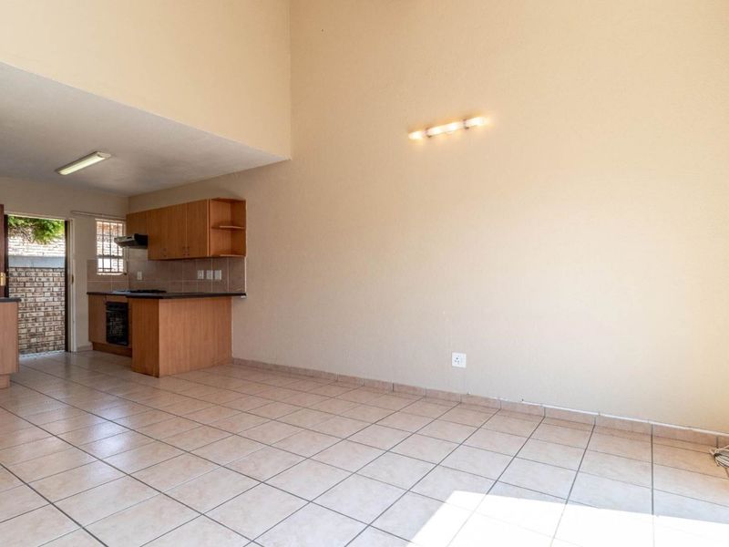 An open-plan living and kitchen area featuring tiled flooring, built-in cabinetry, and a functional kitchen layout with direct access to an outdoor space.