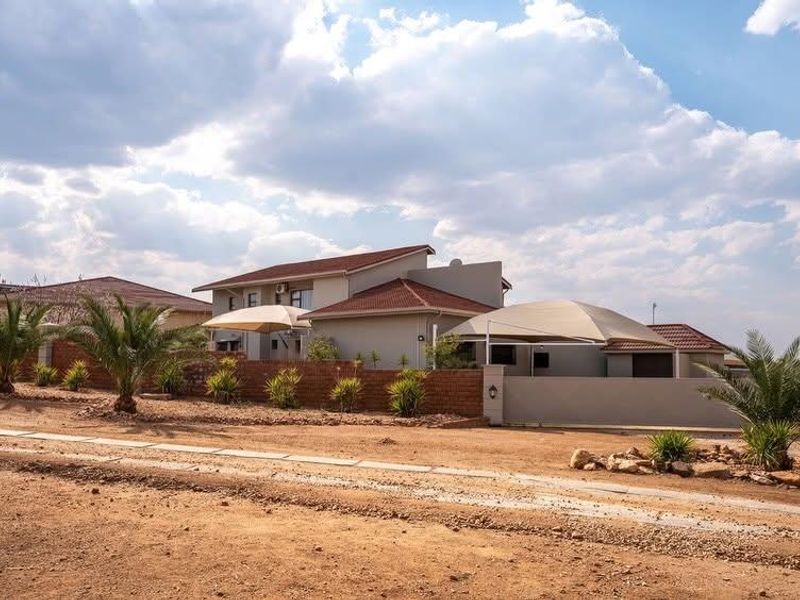 Front exterior view of a residential house featuring a tiled roof, brick boundary wall, and installed shade sail structures over the driveway area.
