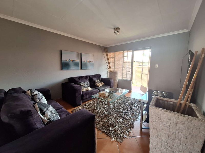A comfortable living room featuring tiled flooring, steel-framed windows, and direct access to an outdoor area through a glass-panelled door.