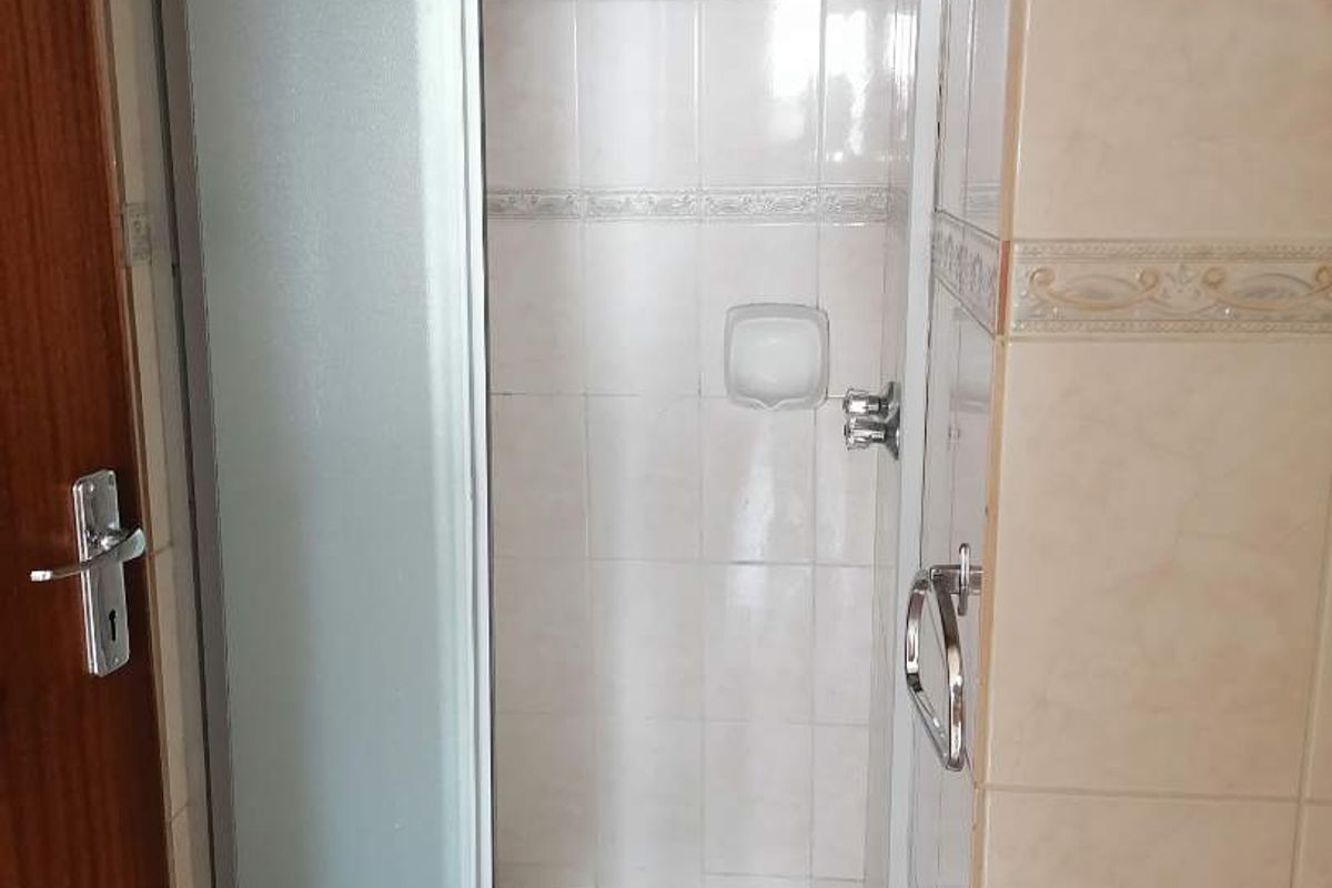 A functional bathroom shower enclosure featuring tiled walls, a standard shower head, and a sliding glass door.
