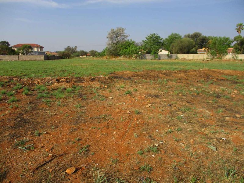 A vacant residential plot featuring open grass and soil, enclosed by perimeter boundary walls in a suburban setting.